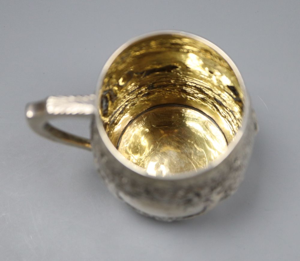A George III silver barrel shaped christening mug, embossed with figures at play in woodland scene,